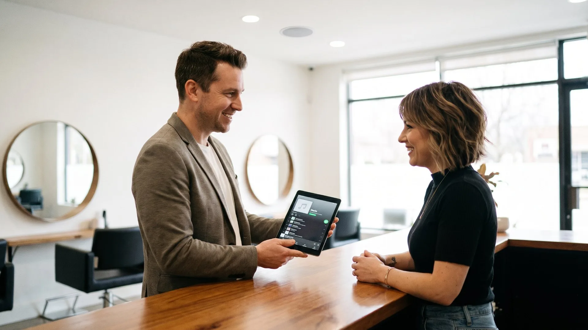 Music consultant showing a playlist on a tablet to a hair salon owner at reception